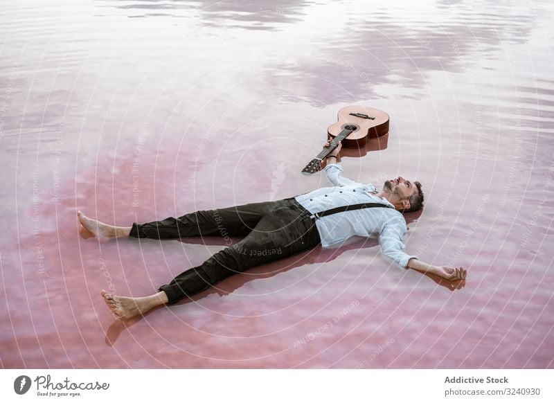 Im Wasser liegender Mann mit Gitarre am Meer ruhen Seeküste stilvoll auf dem Rücken liegend fliegend MEER Sandbank weißes Hemd Hosenträger verträumt friedlich