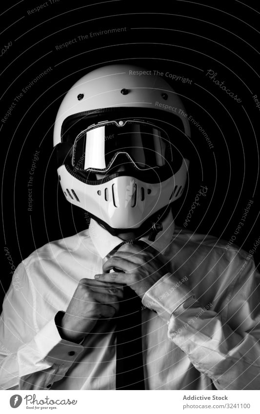 Stylischer Fahrer mit Helm und Brille, der die Krawatte im Studio anpasst Mann Schutzhelm Rennfahrer weißes Hemd starren elegant Einstellung extrem Kontrast