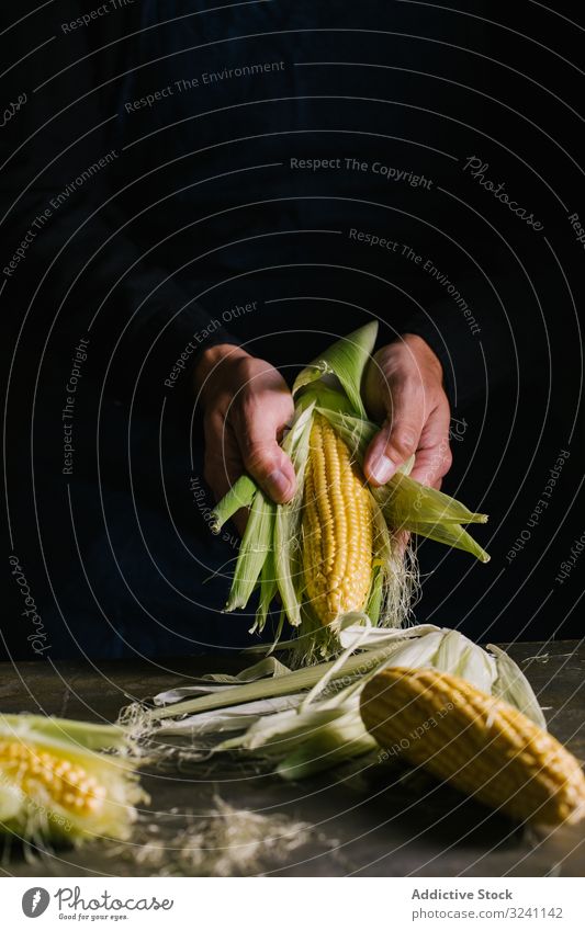 Erntehelfer schält Mais über dem Tisch Person Küche sich[Akk] schälen Blatt rustikal Ackerbau entfernen Lebensmittel heimwärts dunkel Mahlzeit kulinarisch roh