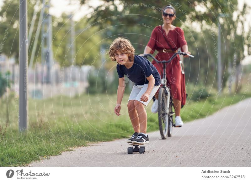 Mutter und Sohn reiten entlang des Parkwegs Mitfahrgelegenheit Weg Skateboard Fahrrad Zusammensein Spaß Familie Glück Junge Frau Kind Sommer Freude froh