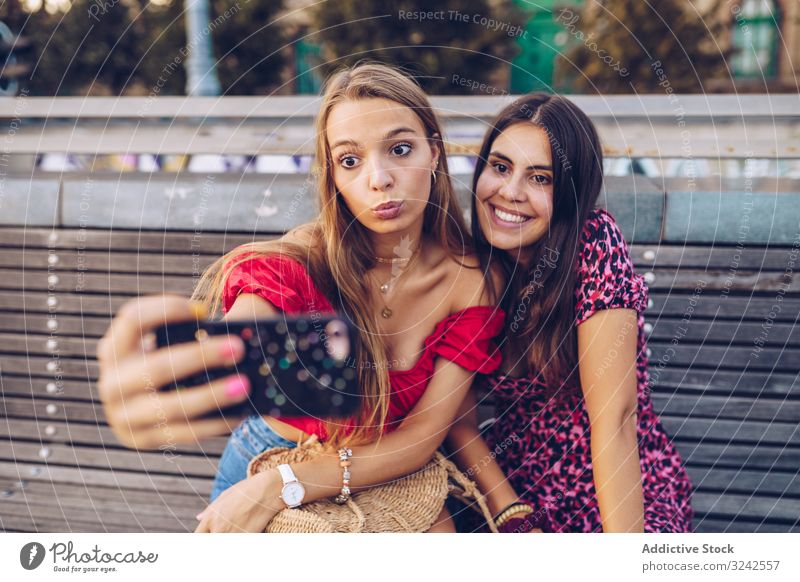 Lachende Frauen, die auf einer Holzbank auf der Straße Selbstgefälligkeit üben Selfie Bank reisen Großstadt Gedächtnis hölzern benutzend Architektur Gebäude
