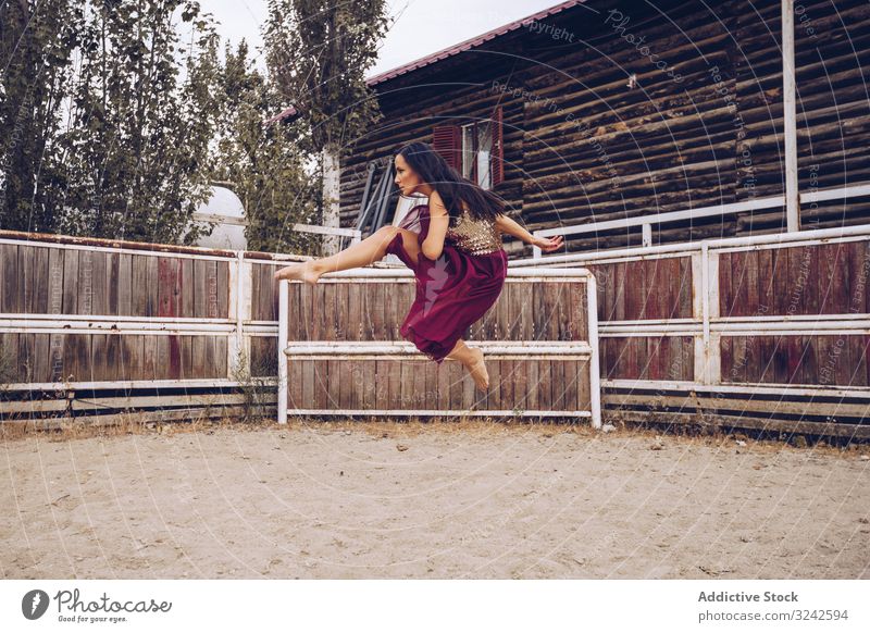 Ausdrucksstarke Frau in farbenfrohem Rock tanzt auf ländlicher Koppel Tanzen Sattelkammer durchsichtig künstlerisch springen Bein hoch Sand Gehege Scheune