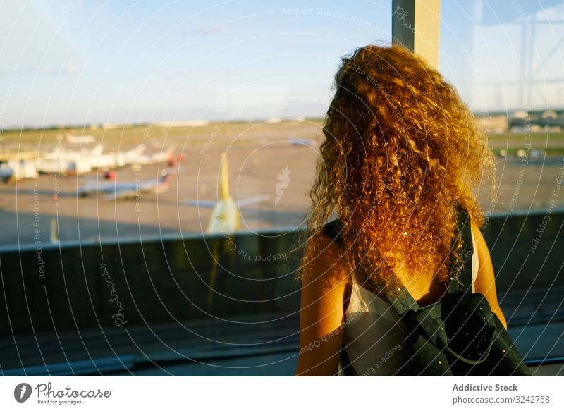 Junge Frau betrachtet nachdenklich Flugzeuge durch Fenster im Sonnenlicht träumen Flughafen Saal Inspiration Freiheit Vorfreude beobachten reisen Rucksack