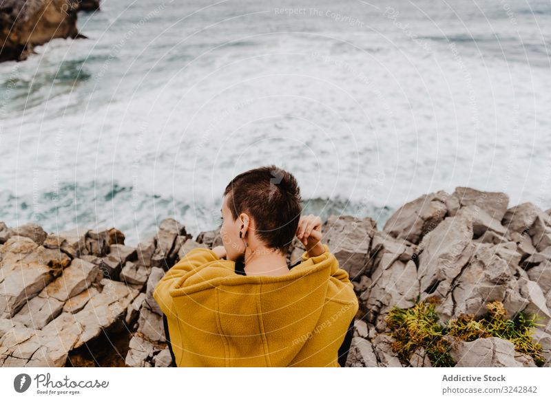 Frau in gelbem Kapuzenpulli an steiniger Küste Einsamkeit Ufer reisen winken Stein zuschauend träumen Harmonie Kontemplation einsam nachdenklich MEER Meer