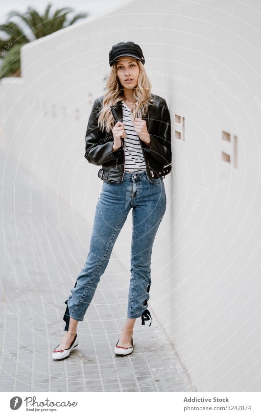 Stilvolle Frau lehnt selbstbewusst an weißer Wand stylisch cool urban trendy Lederjacke provokant Jeansstoff lockig Lifestyle lässig langhaarig modern