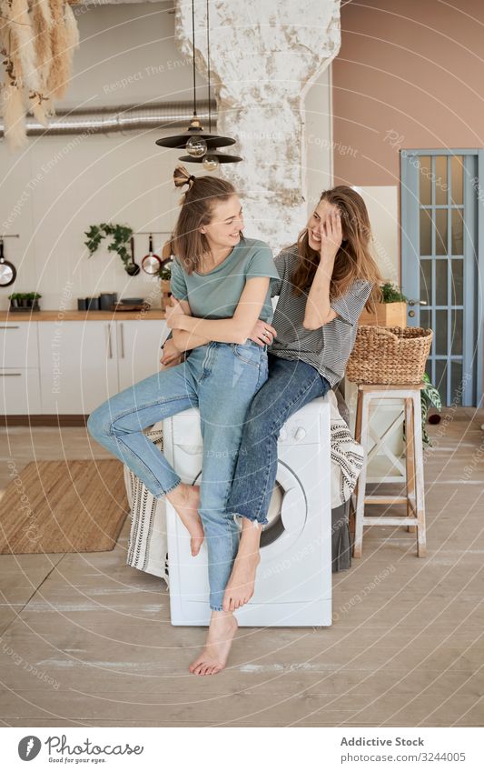 Lachende Freundinnen sitzen auf der Waschmaschine im Haus heimwärts Spaß Paar heimisch Frauen Freizeit Umzug Liebe räkeln Barfuß Zusammensein Komfort Hausarbeit