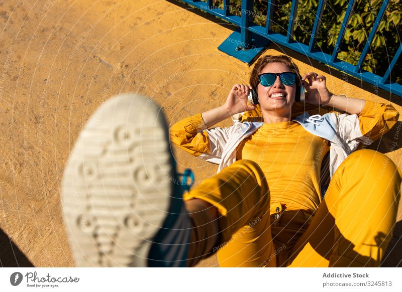 Stilvolle junge Frau in lebhafter Kleidung, die auf der Straße Musik genießt Kopfhörer farbenfroh gelb urban hell blau pulsierend tausendjährig trendy genießen
