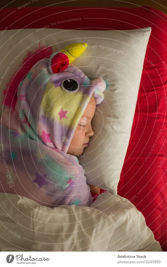 Mädchen im Einhornpyjama schläft im Bett Kind schlafen Pyjama kigurumi Decke rot weiß träumen Lügen niedlich wenig Kindheit Nacht Schlafenszeit heimwärts