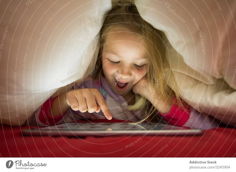 Mädchen benutzt Tablette unter einer Decke Bett Tierhaut benutzend zuschauend Spielen Schlafenszeit Pyjama Lügen Kind Glück Spaß positiv genießen rot weiß