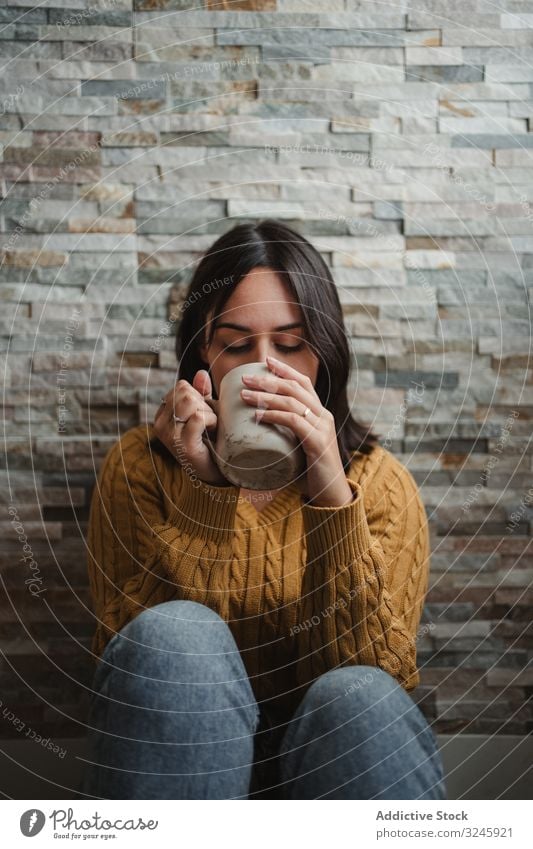 Frau trinkt zu Hause heißen Tee trinken Becher Pullover Kaffee heimwärts sitzen Stock Jeanshose Tasse Getränk jung Halt sich[Akk] entspannen genießen Erholung