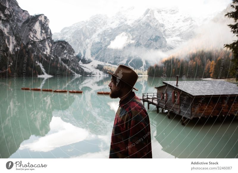 Ruhender Mann in Freizeitkleidung, der sich an Aussichten in der Nähe von See und Bergen erfreut Tourismus Haus Wasser Boot Nebel wolkig reisen Landschaft