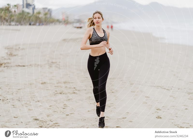 Läuferin in modischer Sportkleidung joggt an ruhiger, sandiger Küste Frau Joggen Strand springend Sommer Gesundheit ausarbeitend Übung Meer Aktivität Training