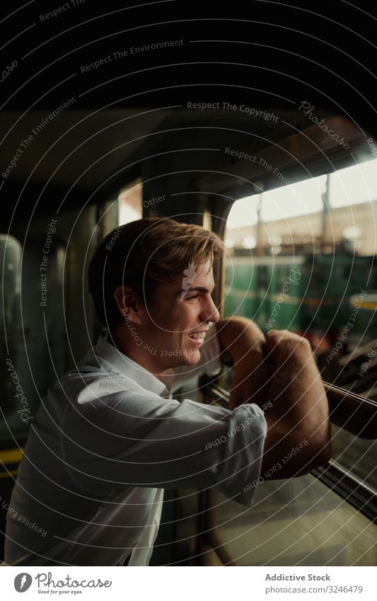 Fröhlicher Reisender schaut aus dem Zugfenster Mann reisen Fenster Lächeln Station Eisenbahn ruhen stoppen Verkehr männlich jung retro altehrwürdig Ausflug