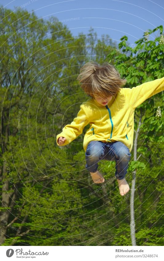 kind springt hoch springen sprung Dynamisch Bewegung aktiv sportlich Sport Spielen Spielplatz gelb grün Bäume Barfuß spass Trampolin Junge Jacke Sommer hüpfen