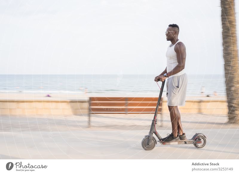 Cooler erwachsener schwarzer Mann fährt Roller auf der Straße Mitfahrgelegenheit Afrikanisch ethnisch Elektroroller trendy cool Spaß Laufwerk elektrisch
