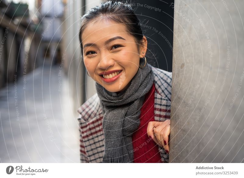 Fröhliche Asiatin ruht weiblich in legerer Kleidung und schaut aus moderner Gebäudewand an der Stadtstraße Frau Straße reisen Tourist Tür Peer schauen Sie