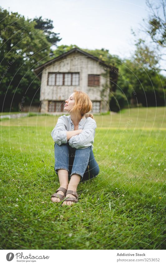 Zufriedene Frau sitzt auf Gras auf dem Land Landschaft Haus genießen Feld Wiese Windstille friedlich Inhalt nachdenklich sorgenfrei ländlich Dorf Rotschopf