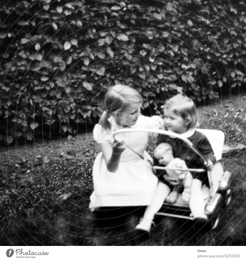 Beziehungspflege • Zwei Mädchen mit Kinderwagen und Puppe vor einer Hecke feminin Kleinkind 2 Mensch Park Wiese Wege & Pfade Kleid blond langhaarig Zopf