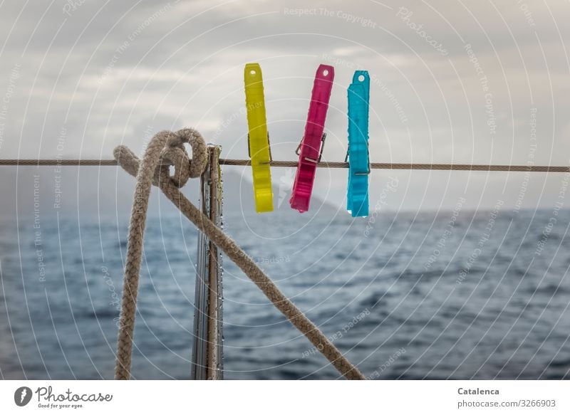 Drei Wäscheklammern an einer Bootsreling hoffen auf besseres Wetter schlechtes Wetter Wassertropfen Regen nass Meer Reeling Segelyacht Wolken blau rot gelb