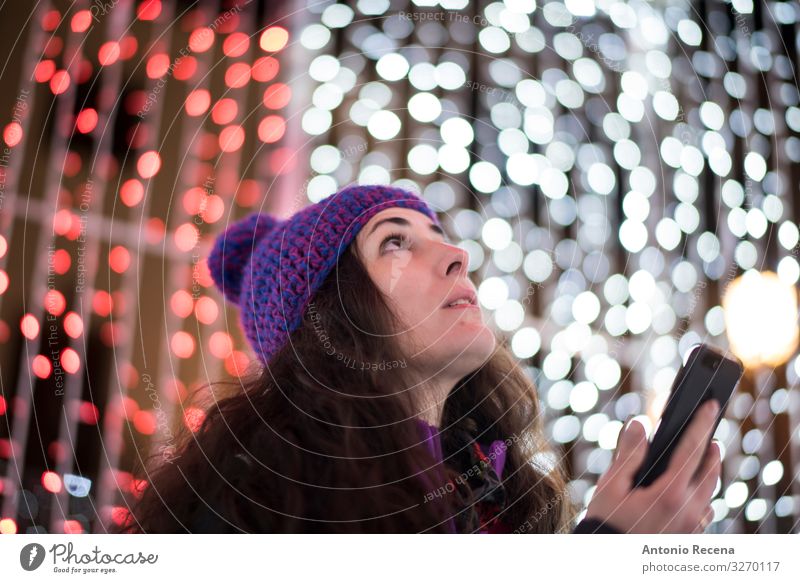 Frau mit Smartphone, die Weihnachtslichter sieht Freude Winter Telefon PDA Technik & Technologie Internet Erwachsene Hut fantastisch Gefühle Weihnachten