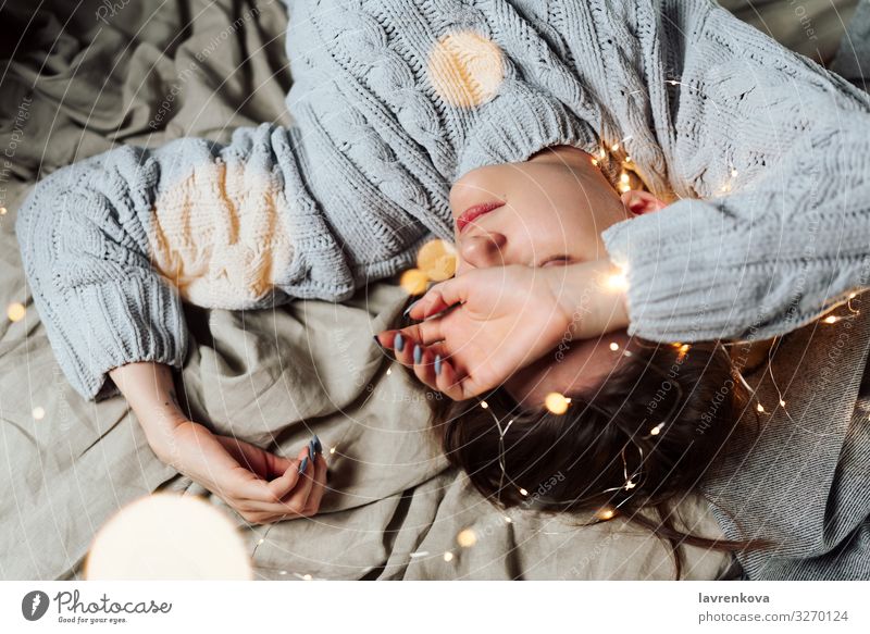 Junge weiße Frau im Bett liegend mit Lichterkette und Bokeh um, flacher selektiver Fokus Bettwäsche Unschärfe Kaukasier Weihnachten & Advent bequem gemütlich