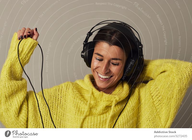 Verspielte junge Frau, die im Studio Musik hört zuhören Kopfhörer anhaben gelb Pullover genießen stereo spielerisch Spaß benutzend Atelier Klang Wiedergabeliste