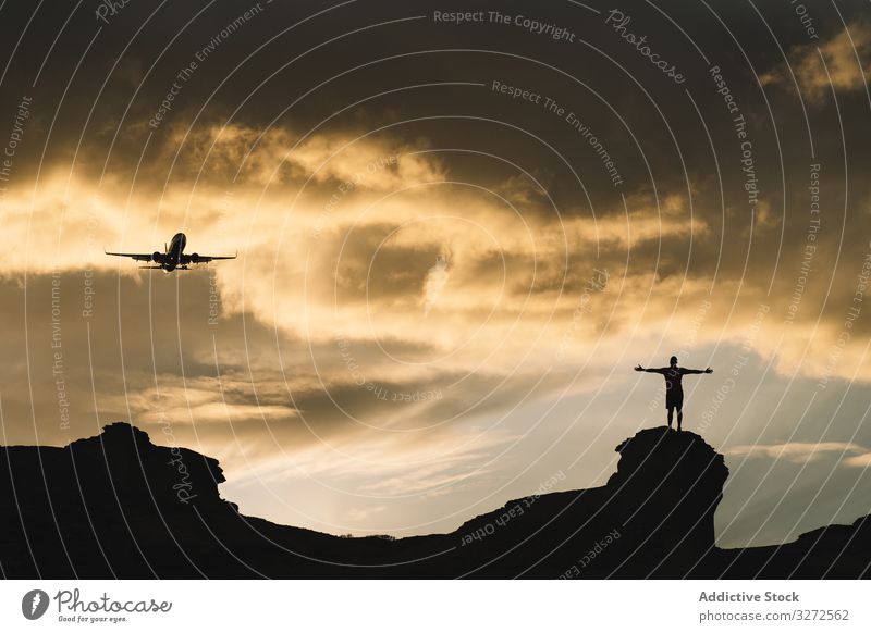 Menschliche Silhouette auf einem Hügel, der sich beim Anblick von Flugzeugen am Himmel erfreut Fluggerät Stehen Berge u. Gebirge genießen Freude Freiheit