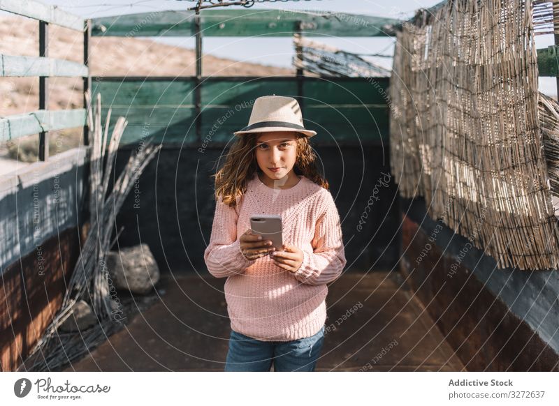 Fokussiertes Mädchen benutzt Smartphone auf dem Land Lastwagen benutzend ruhen fokussiert Konzentration PKW Roséwein Trägerkleid lässig Strohhut achtsam