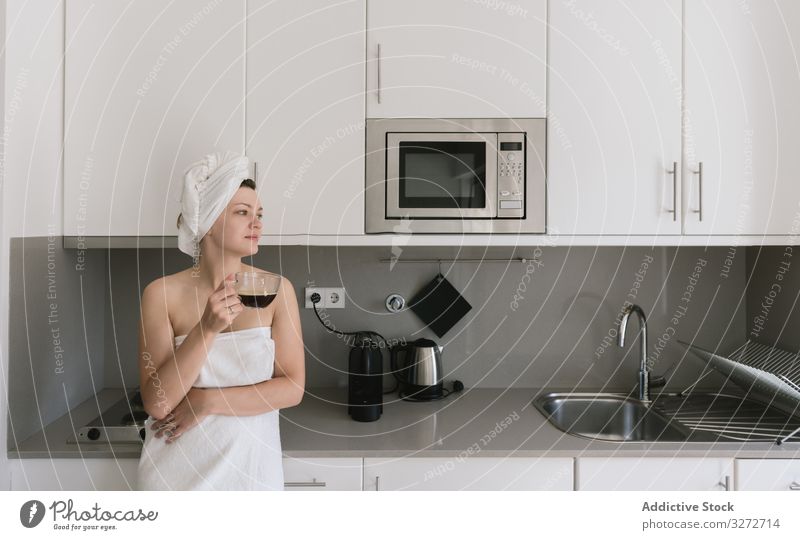 Fröhliche erwachsene Frau genießt freien Tag bei einem heißen Getränk nach dem Bad in einer Wohnung mit einfacher Inneneinrichtung Kaffee Morgen Küche Glück