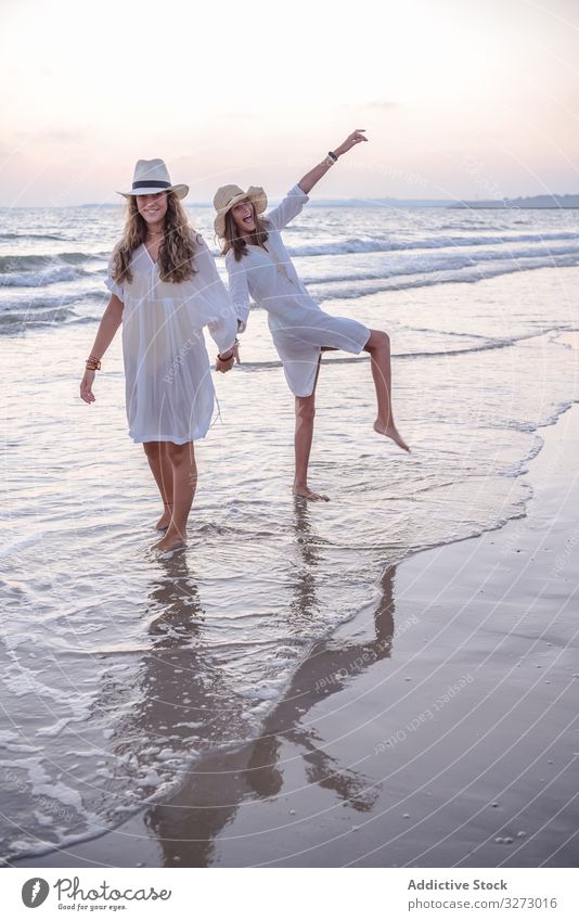 Lächelnde Freundinnen in Sommerkleidung barfuss im Wasser am Strand Frauen MEER Barfuß reisend Seeküste charmant Urlaub Hut lockig Feiertag Zusammensein