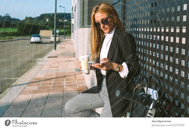 Geschäftsfrau, die ihr Handy benutzt und mit ihrem Roller Kaffee trinkt Lifestyle Stil schön Freizeit & Hobby PDA Mensch Frau Erwachsene Straße Mode