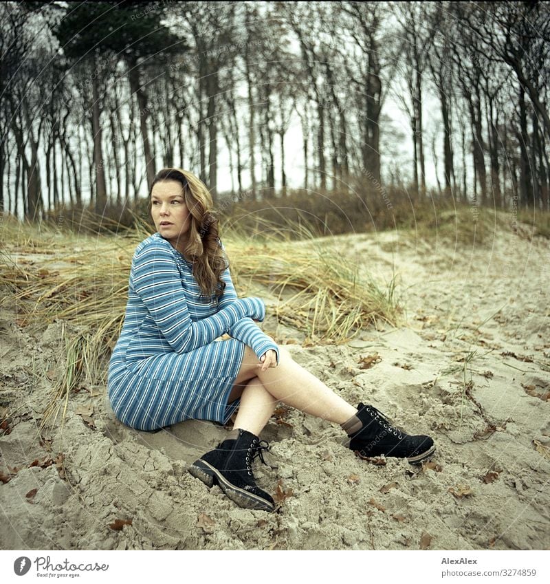 Junge Frau sitzt auf Düne Stil Freude schön Leben Jugendliche Erwachsene 18-30 Jahre Landschaft Blume Gras Sträucher Strand Kleid Wanderschuhe brünett