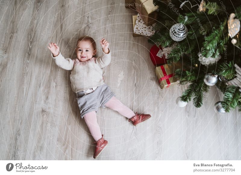 süßes Mädchen, das auf dem Boden beim Weihnachtsbaum liegt lügen Freude Glück niedlich Baby ein Jahr dekorierend Weihnachten & Advent Baum
