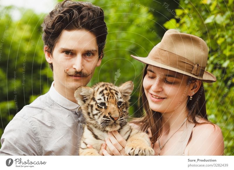 Ein Mann und eine Frau halten Tigerjunge wütend Tier Hintergrund Bengalen schwarz Katze schließen Nahaufnahme Esser Gesicht Wald Freund Glamour Hut Kopf Halt
