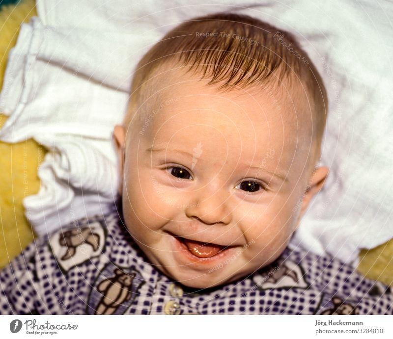 auf einem Lammfell liegendes Baby lächelt Freude Glück Junge Lächeln weich Geburt Born Ausdruck Blick lügen Zunge Farbfoto Tag