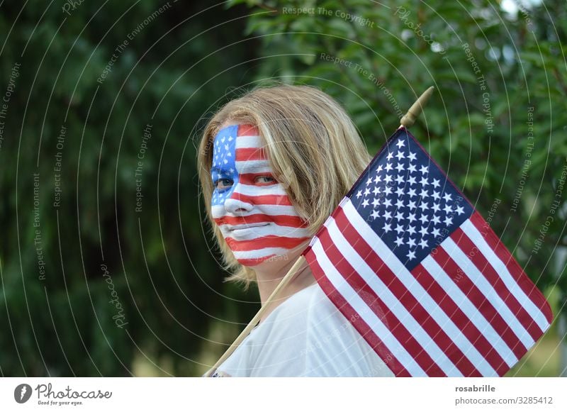 Flagge zeigen | wörtlich genommen | patriotische junge blonde Frau mit amerikanischer Fahne und Flagge aufs Gesicht gemalt im Freien hofft auf den Sieg ihrer Fußballmannschaft