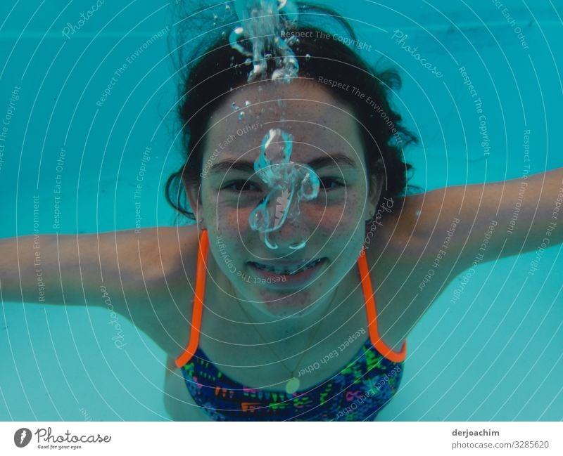 Ein Mädchen unter Wasser blickt zum  Fotografen. Sie lacht und es macht Blub blub.. Freude sportlich Leben Schwimmbad Wassersport Schwimmen & Baden