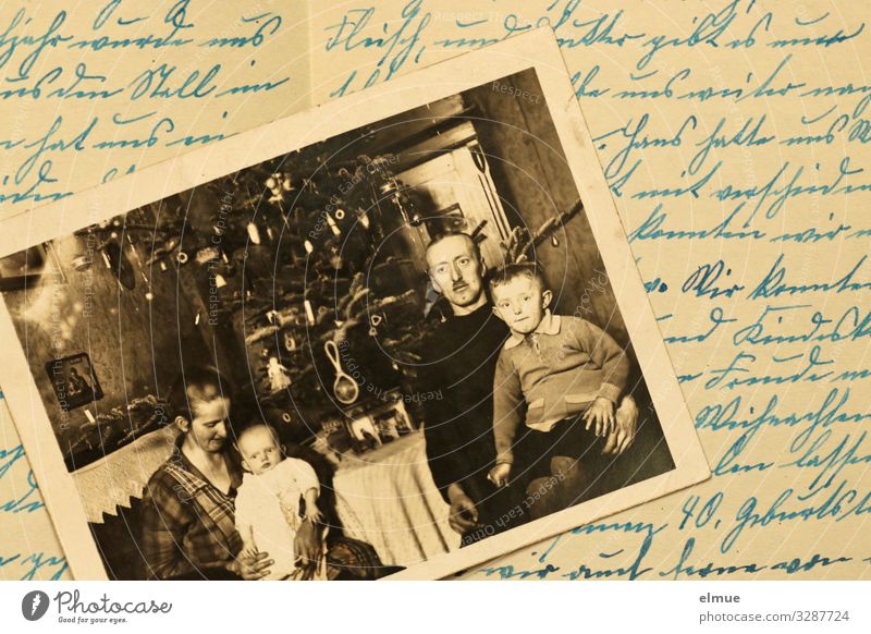 ein altes Papierbild aus den 1920er Jahren zeigt eine Familie mit zwei Kleinkindern vor einem geschmückten Weihnachtsbaum - auf einem alten Schriftstück in altdeutscher Handschrift liegend