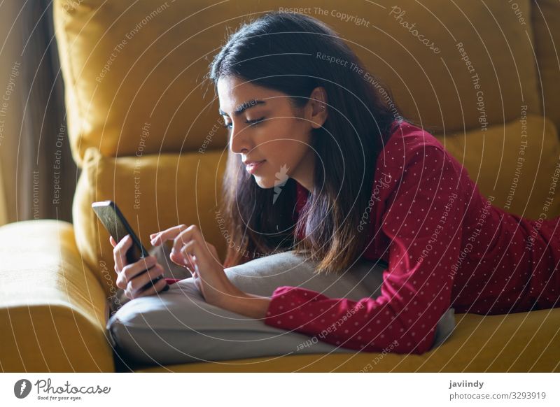 Persische Frau, die zu Hause ihr Smartphone benutzt Lifestyle Haare & Frisuren Erholung Freizeit & Hobby lesen Winter Wohnung Sofa Wohnzimmer Telefon PDA
