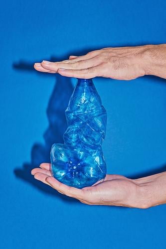 Zwei Hände, die eine Plastikflasche auf blauem Hintergrund drücken Flasche Lifestyle kaufen sparen Strand Meer Industrie Hand Umwelt Verpackung Kunststoff