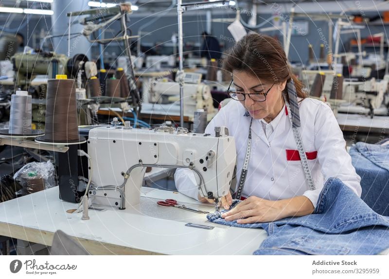 Frauenhände in einer Textilfabrik beim Nähen auf einer Industrienähmaschine. Fabrik Bekleidung Herstellung Arbeiter Maschine Hände Gewebe Hose Blue Jeans Beruf