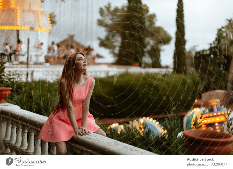 Junge Frau in rosa Kleid sitzt auf einem Zaun im Vergnügungspark Jahrmarkt romantisch sinnlich Karussell Teenager Mode Entertainment Stil trendy tausendjährig