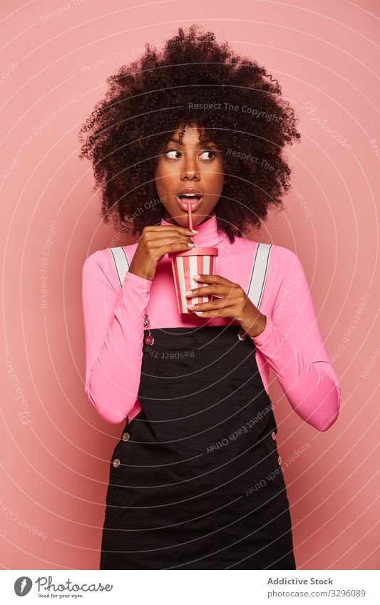 Glückliche schwarze Frau mit Einweg-Getränkebecher vor rosa Hintergrund trinken Tasse Stroh Afroamerikaner Lachen Einwegartikel heiter stehen gestikulieren