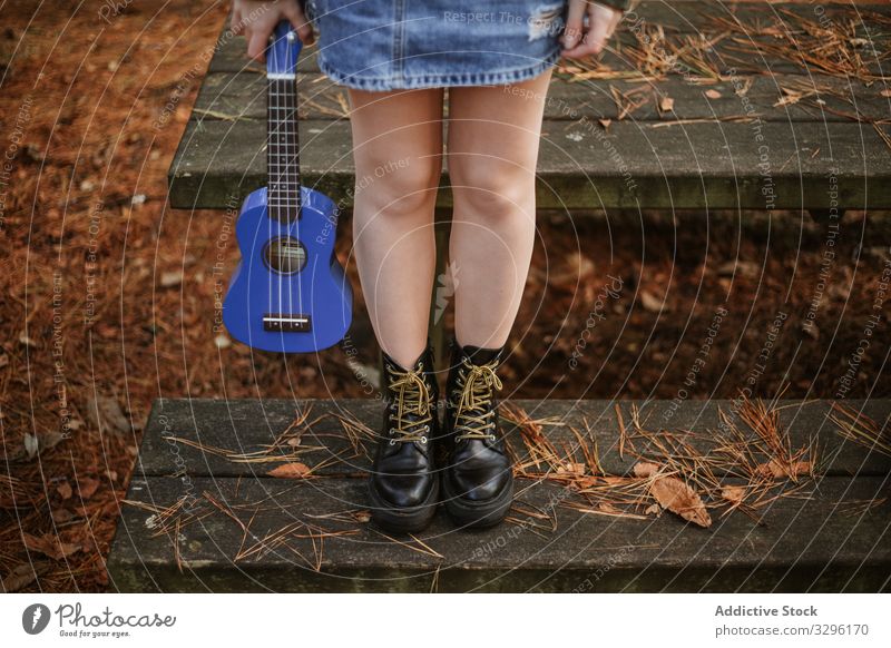 Junge Frau mit Ukulele auf Holztreppe im Park Teenager Gitarre Herbst Treppe Stiefel Musik allein Instrument klein Gerät Schuhe Hand Kiefernadeln