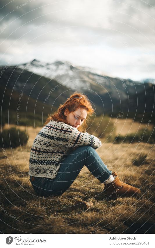 Rothaarige Frau, die nachdenklich auf einer Wiese in den Bergen sitzt gemütlich Berge u. Gebirge Landschaft besinnlich warm Pullover bequem Mode Komfort