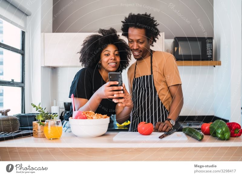 Ein Afro-Paar, das zusammen kocht und zu Hause telefoniert. Lifestyle Glück Freizeit & Hobby Wohnung Küche Telefon Handy Frau Erwachsene Mann Afro-Look Lächeln
