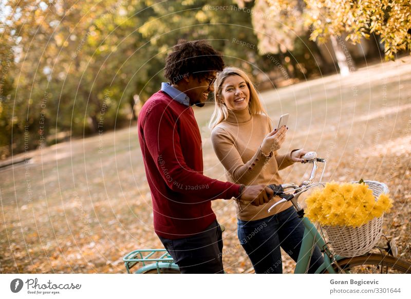 Mehrrassiges Paar mit Fahrrad im Herbstpark stehend Lifestyle Glück schön Freizeit & Hobby Telefon PDA Frau Erwachsene Mann Blume Blatt Park Lächeln lachen