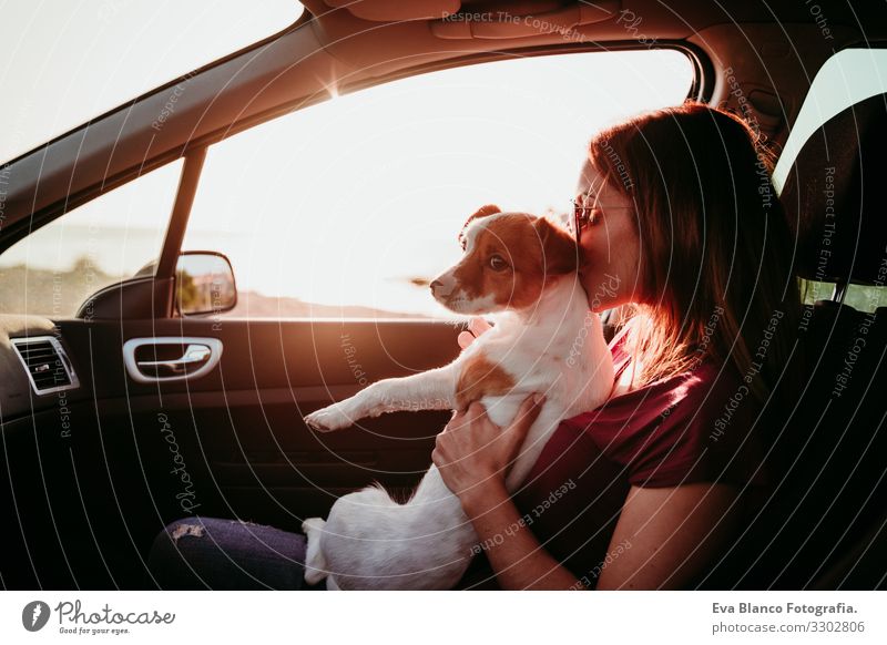 junge Frau und ihr süßer Hund im Auto bei Sonnenuntergang. reisekonzept PKW Ferien & Urlaub & Reisen Tourismus Zusammensein Liebe Umarmen Landschaft Strand