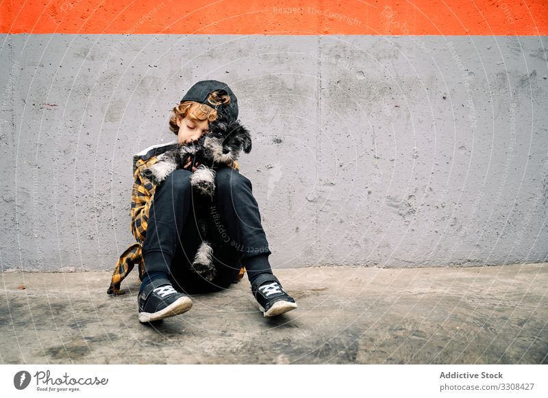 Junge mit Welpe sitzt neben Betonwand Kind Hund Straße sitzen Gebäude Zuneigung Pflege wenig züchten Eckzahn Reinrassig Tier kuscheln heimisch freundlich
