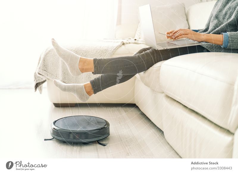 Frau sitzt auf Sofa mit Füßen auf Roboter-Staubsauger Vakuum Raumpfleger robotisch klug heimwärts Technik & Technologie Stock Drahtlos Vorrichtung Maschine
